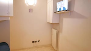 Een kleine, eenvoudig ingerichte kamer met een bed, een aan de muur bevestigde televisie en een radiator.