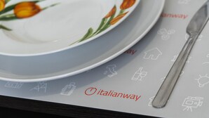 Une assiette blanche ornée de tulipes orange et une cuillère en argent sont posées sur une table. Sur la table se trouve également un guide imprimé, illustré d’icônes telles qu’une maison, une bouteille et un appareil photo.