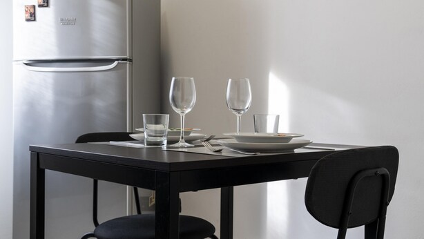 Une table à manger avec deux verres à vin, des assiettes et des couverts, une chaise, et un réfrigérateur, le tout dans un décor de cuisine moderne.