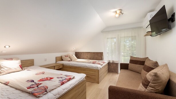 Ett modernt hotellrum med en stor säng, en mindre säng, en soffa och en tv som är monterad på väggen.
