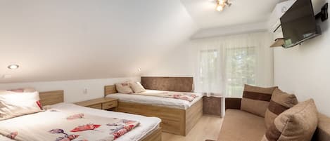 A modern hotel room with a large bed, a smaller bed, a sofa, and a TV mounted on the wall.