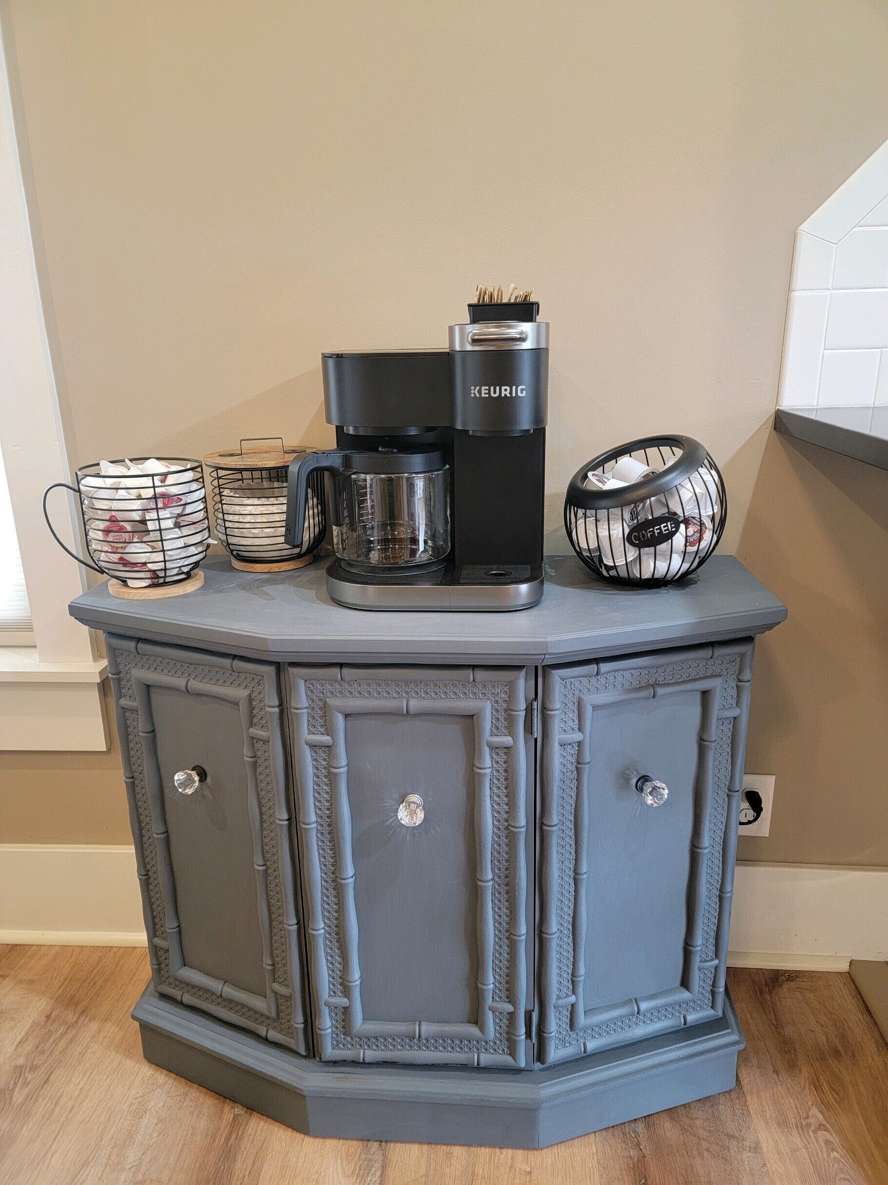 Een kitchenette met een koffiezetapparaat, een koffiekan en een koffiemolen op een grijs kastje.