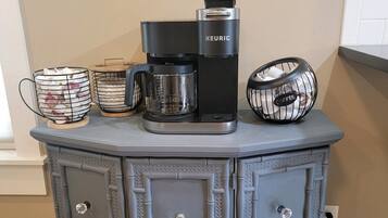Een kitchenette met een koffiezetapparaat, een koffiekan en een koffiemolen op een grijs kastje.