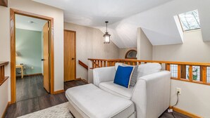 Een gezellige woonkamer met een witte bank, een blauw kussen en een houten leuning.