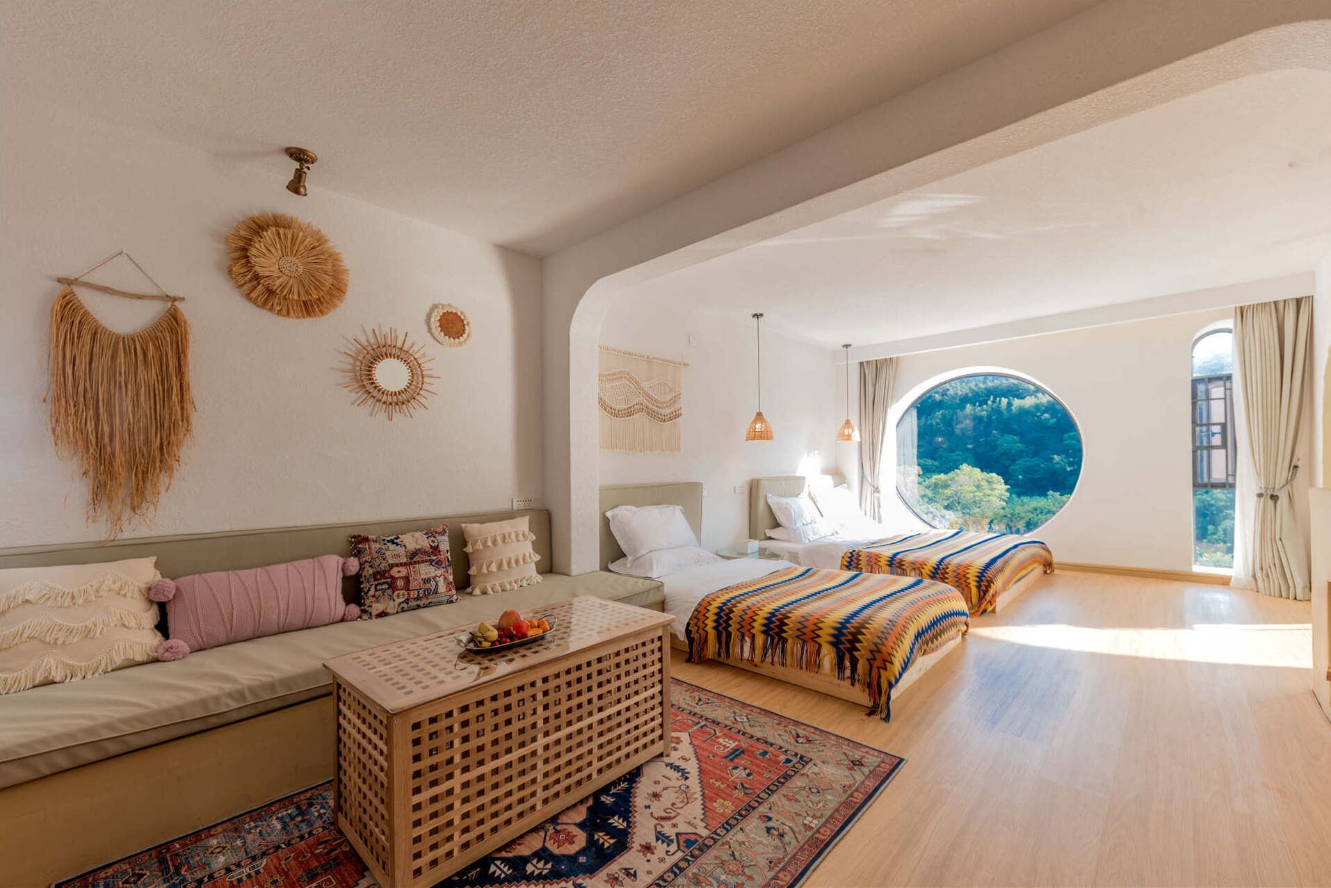 A spacious bedroom with two beds, a large window with a view of greenery, and a cozy seating area with a patterned rug.