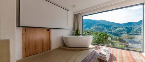 Um banheiro moderno com uma banheira independente, uma janela ampla com vista para as montanhas e uma cama bem arrumada com um cobertor colorido.