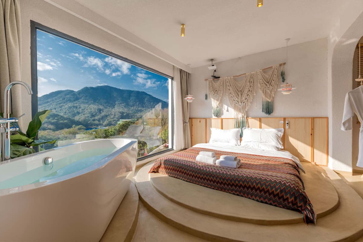 Ein Schlafzimmer mit großem Fenster, einer Badewanne und einem Bett mit gemusterten Betttextilien.