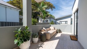 A modern outdoor patio with a beige sofa, potted plants, and a tiled floor. - Belle 4-141 ~ Experience a relaxing escape! (Gerringong)