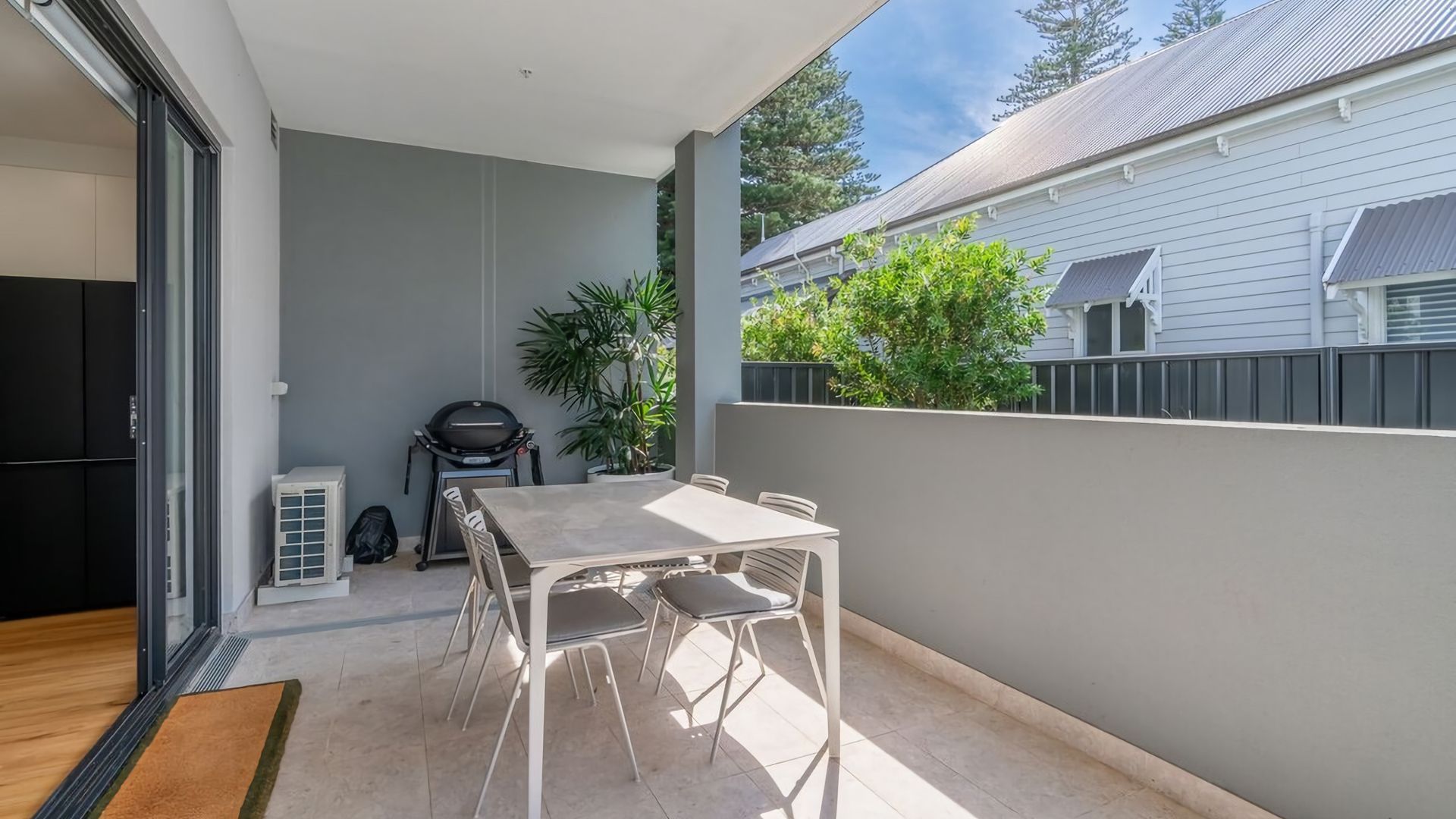 A patio with a table and chairs, a barbecue grill, and a potted plant.