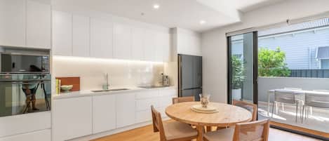 A modern kitchen with white cabinetry, a built-in microwave, and a stainless steel refrigerator. There is a round wooden dining table with chairs in the foreground.
