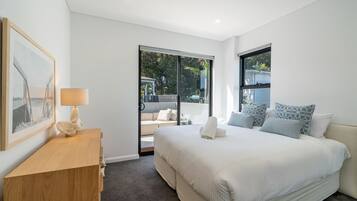 A modern bedroom with a large bed, a bedside table, a lamp, and a view of the outdoors through a sliding door.