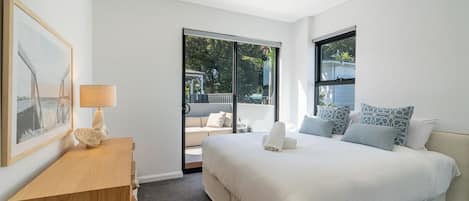A modern bedroom with a large bed, a bedside table, a lamp, and a view of the outdoors through a sliding door.