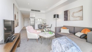 A modern living room with a sofa, a coffee table, and a TV. There is a dining area with chairs and a table. The room has a large window and a painting on the wall. - lovely ap in  heart of chatswood (Chatswood)