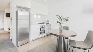 A modern kitchen with white cabinetry, stainless steel appliances, and a round dining table with two chairs. - lovely ap in  heart of chatswood (Chatswood)
