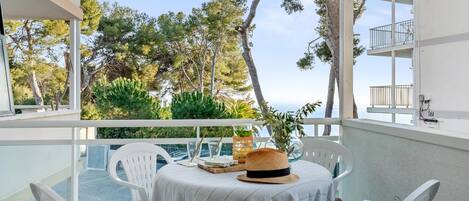 A balcony with a table set for two, overlooking a scenic view of trees and the sea.