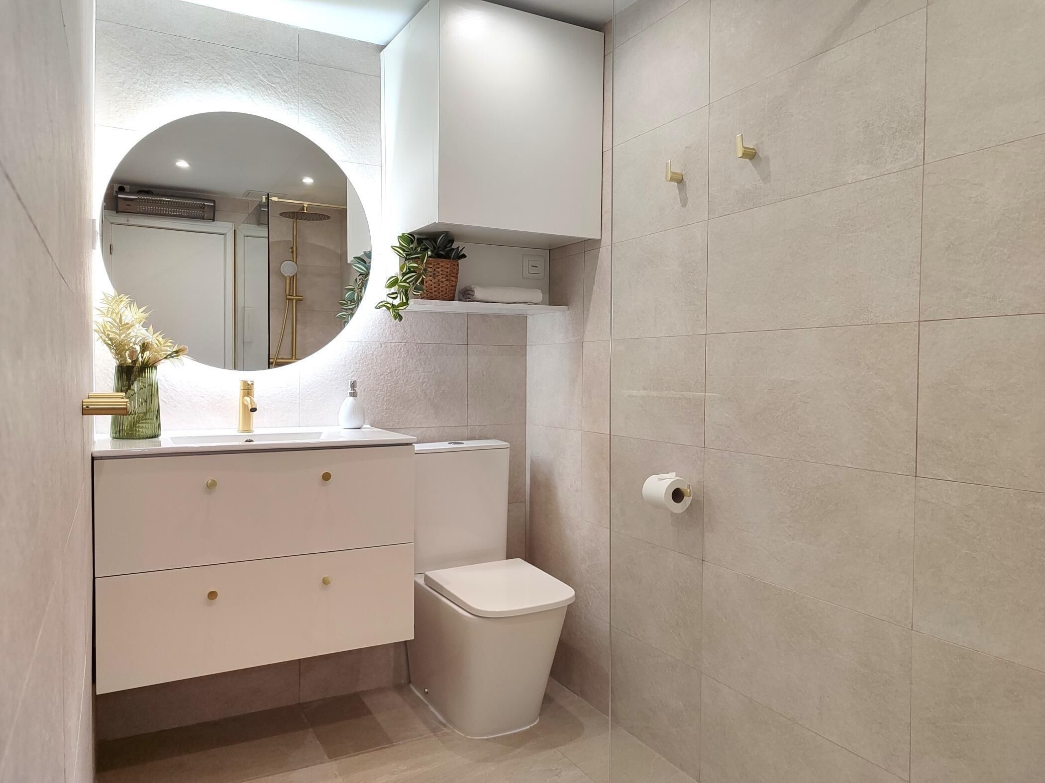 A modern bathroom with a white vanity, a round mirror, a toilet, and a trash bin.