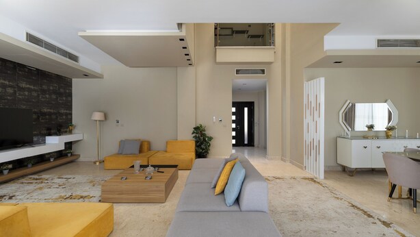 A modern living room with a sofa, coffee table, and a TV. There is a staircase leading to an upper level.