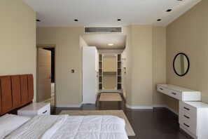 A bedroom with a bed, a bedside table, a dresser, a walk-in closet, and a mirror on the wall. - Villa With Private Pool In Beverly Hills (Sheikh Zayed City)