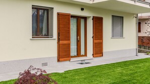A modern two-story house with a well-maintained lawn, wooden shutters on the windows, and a small decorative plant in the front yard. - Apartment Syria by Interhome (Domaso)
