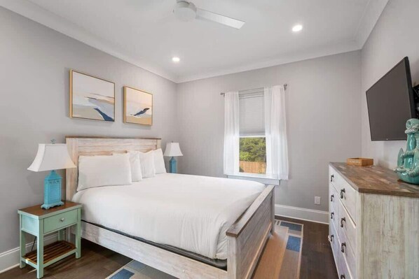 A bedroom with a bed, two bedside tables, a dresser, a TV, and a window with curtains.
