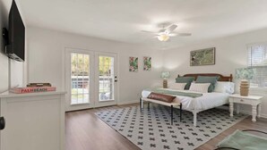 Une chambre à coucher comprenant un lit, un ventilateur de plafond, une fenêtre avec des stores et une porte donnant sur un espace extérieur.