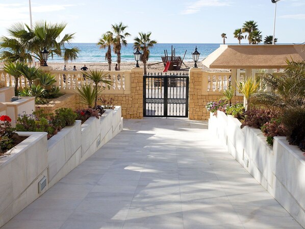A paved pathway leading to a beach with palm trees and a gate.