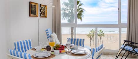 Comedor con una mesa dispuesta para cuatro personas, frente a un amplio ventanal con vista a la playa.