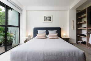 A modern bedroom with a large bed, two bedside tables with lamps, a framed picture on the wall, and a view of greenery through a sliding door. - Spacious apartment in Condesa near Parque México (Ciudad de México)
