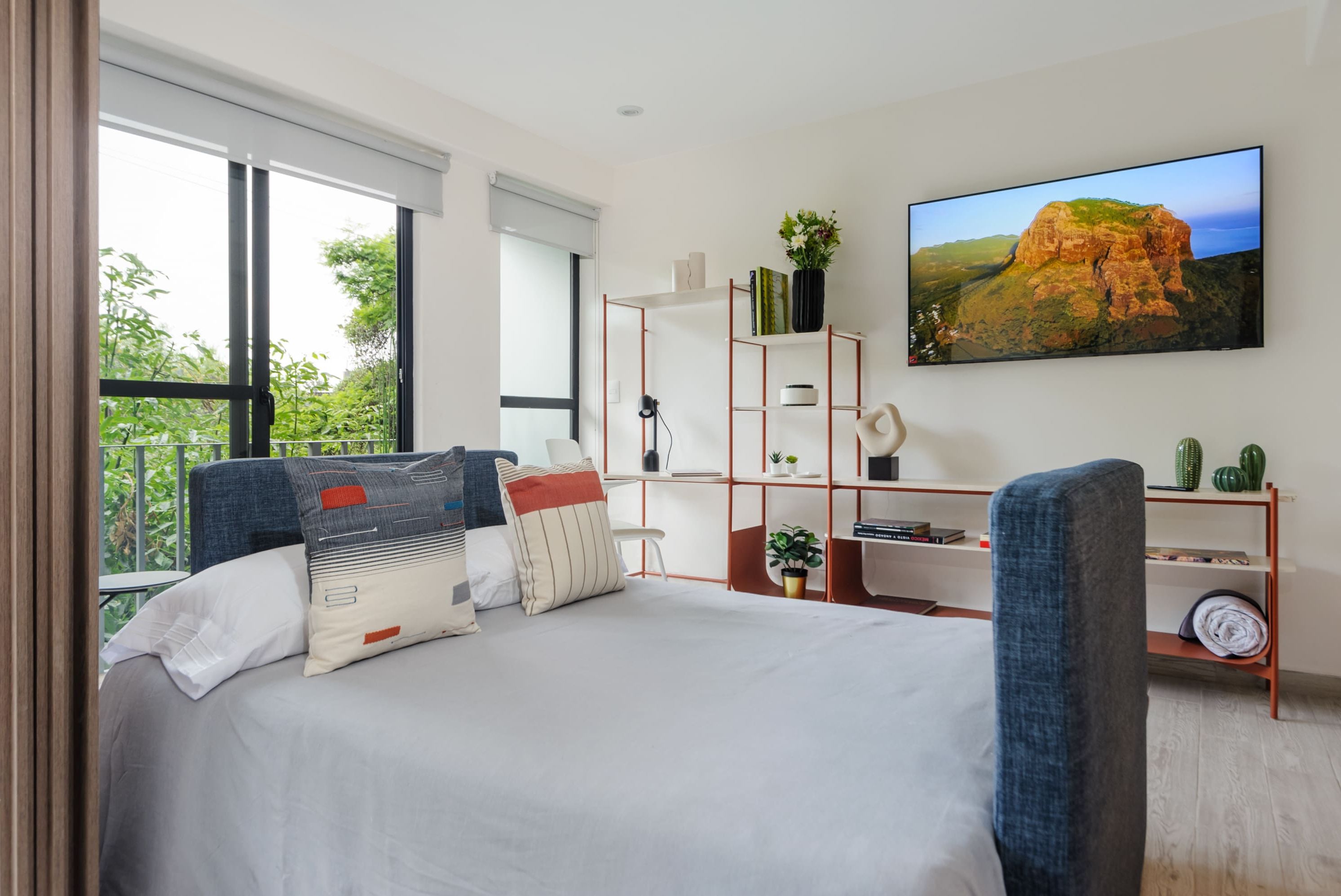 A modern bedroom with a large bed, a desk, and a TV.