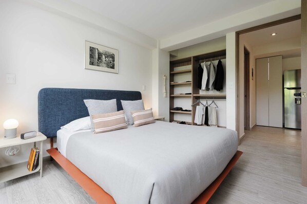 A modern bedroom with a large bed, a bedside table with a lamp, a wardrobe, and a framed picture on the wall.