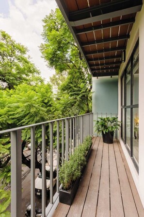 A wooden deck with potted plants, a metal railing, and a view of trees.