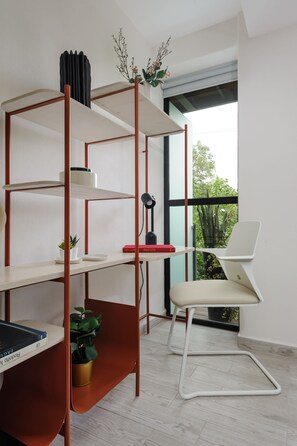 Um espaço de trabalho moderno com uma mesa branca, um livro vermelho, uma planta em vaso e uma cadeira branca.