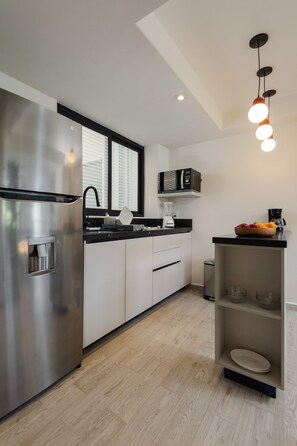 A modern kitchen with a stainless steel refrigerator, white cabinets, a black countertop, a built-in microwave, and a fruit bowl.