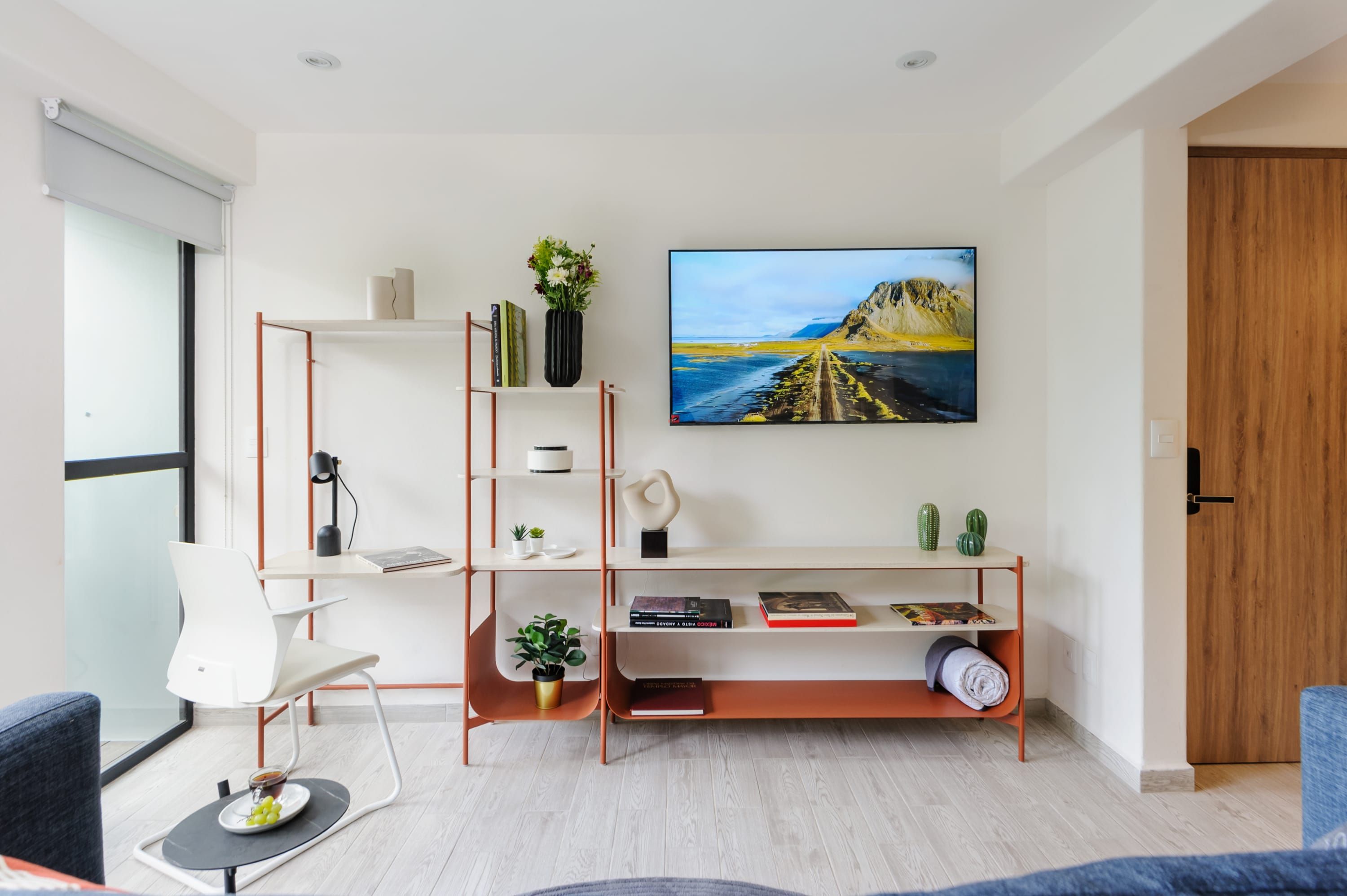 A modern living room with a white sofa, a coffee table with a fruit bowl, a bookshelf, and a large painting on the wall.