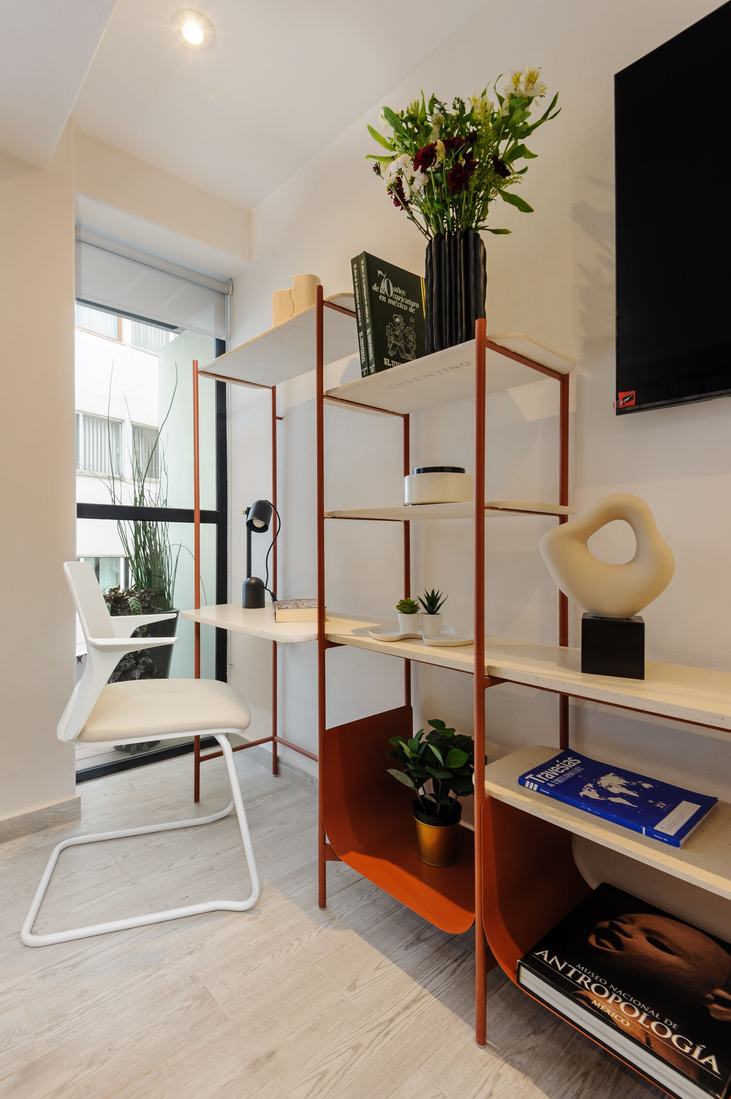 A modern room with a white chair, a bookshelf with books and decorative items, and a potted plant.