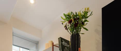 Una habitación moderna con una silla blanca, una estantería con libros y objetos decorativos, y una planta en maceta.