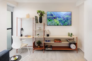 A modern living room with a white chair, a wooden bookshelf, a flat-screen TV, and a small table with a bowl of fruit.