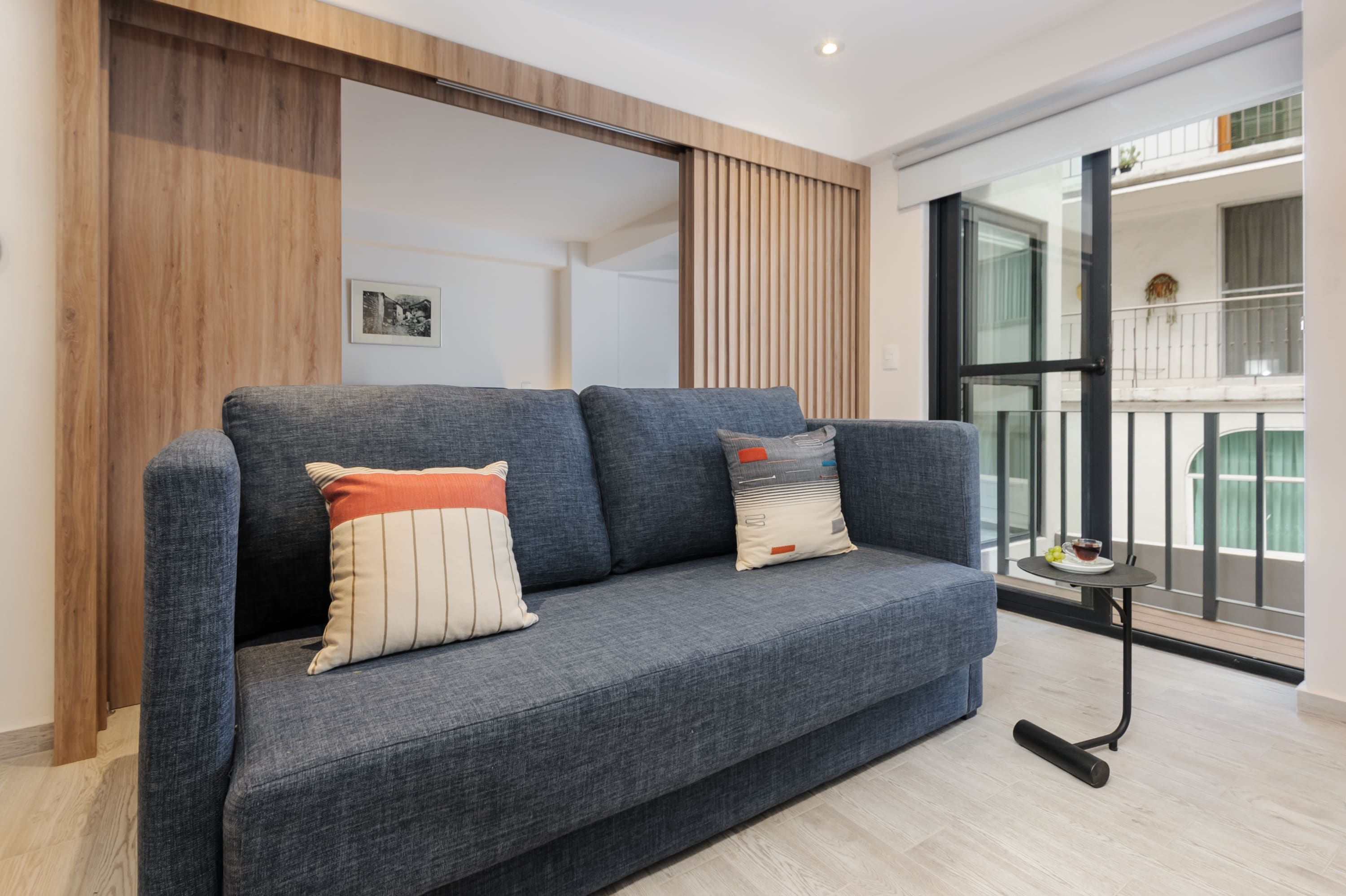 A modern living room with a grey sofa, wooden paneling, and a view of a balcony.