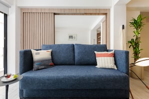 A modern living room with a blue sofa, two decorative pillows, a small table with a glass, and a potted plant. - Brand New Modern Apartment in Condesa (Ciudad de México)
