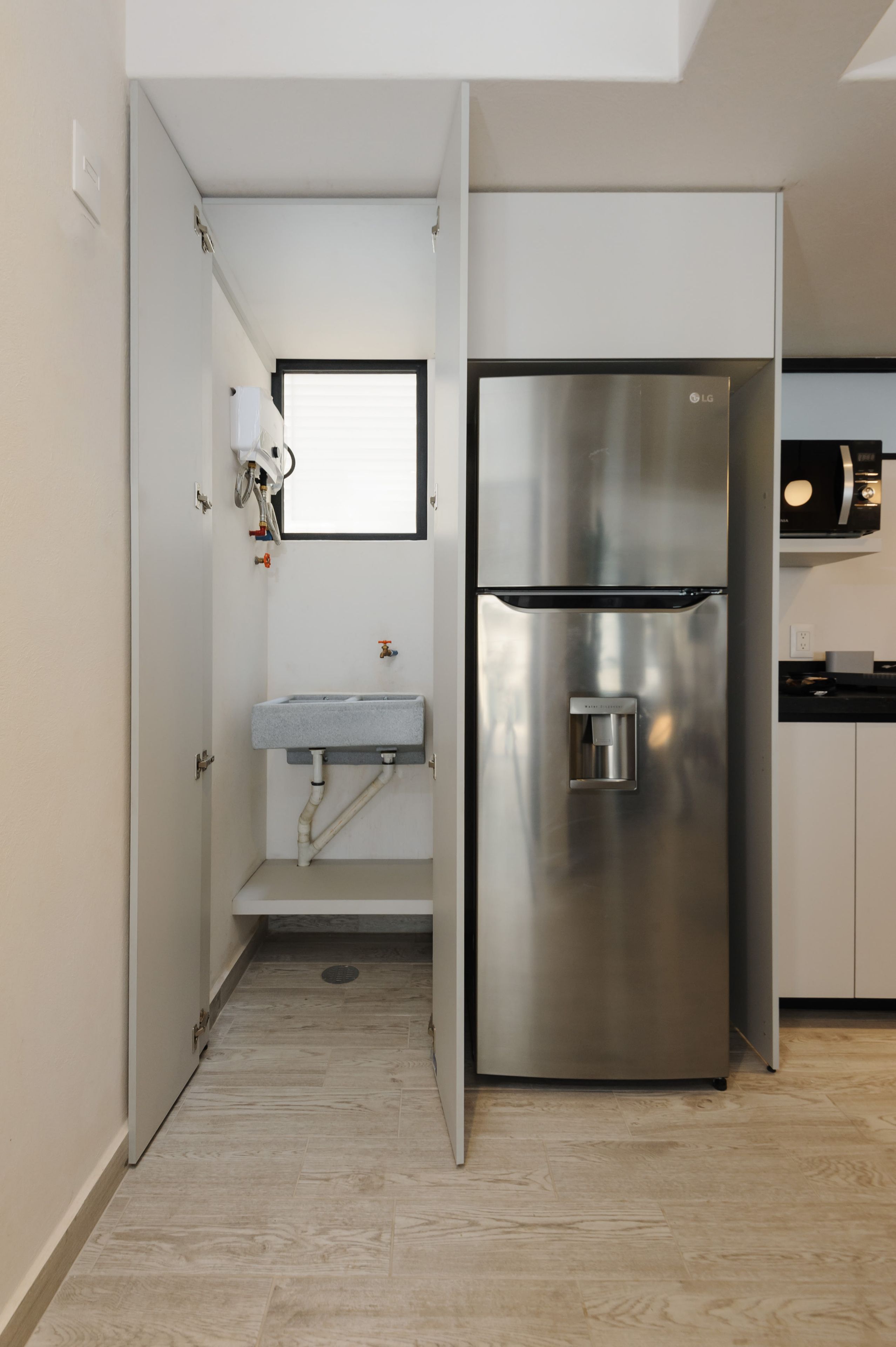 A compact kitchen with a built-in sink, a stainless steel refrigerator, and a microwave.