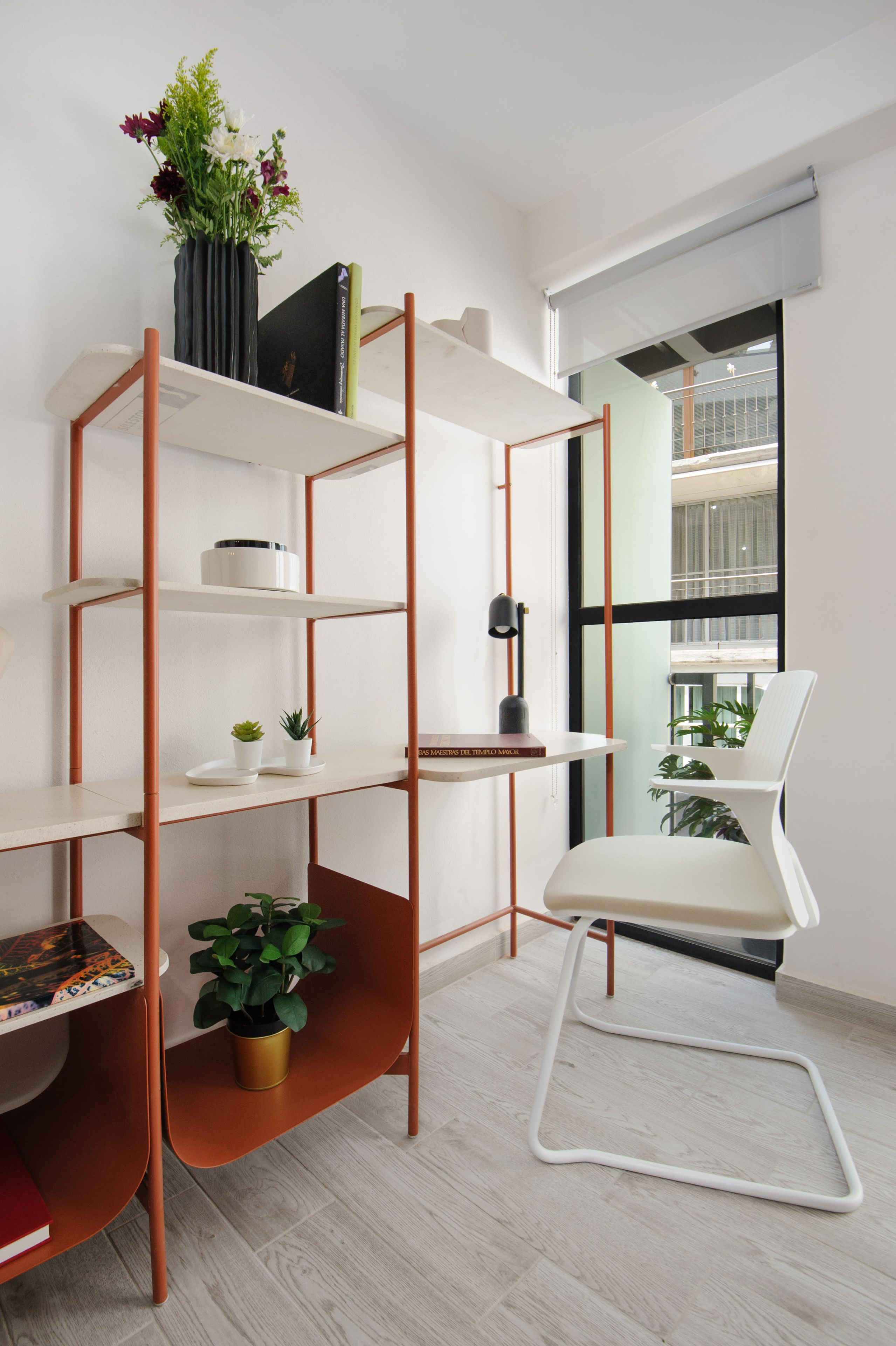 A modern room with a white chair, a bookshelf, and a potted plant.