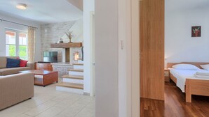 Een moderne woonkamer met een bank, tv en een open haard. Een houten deur leidt naar een slaapkamer met een bed.