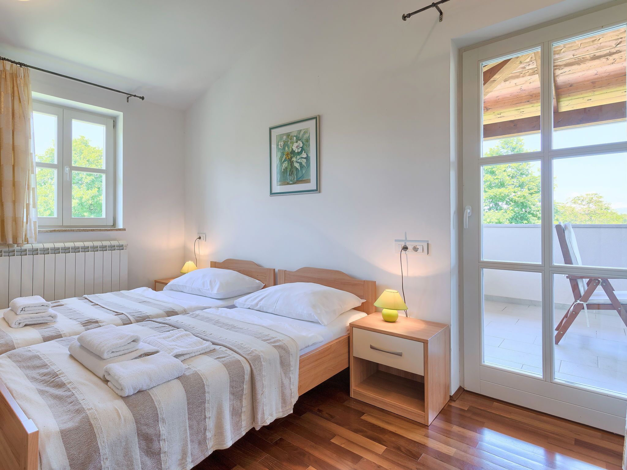 A bedroom with a bed, bedside tables, a radiator, a window, and a door leading to an outdoor area.