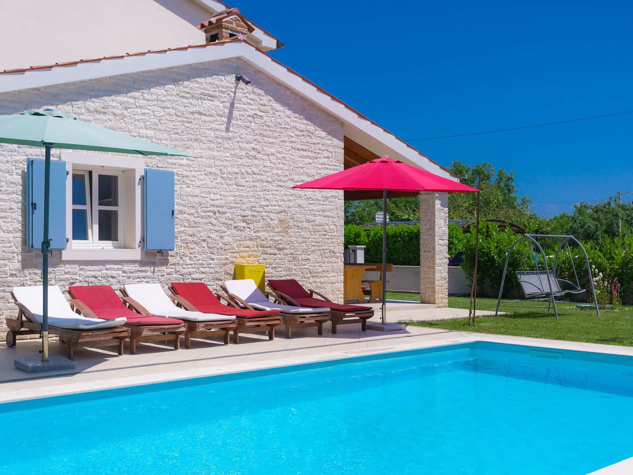 A poolside area with lounge chairs and a red umbrella.