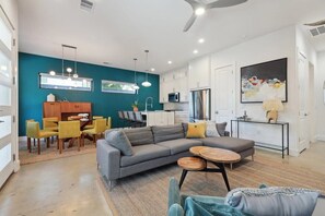 Ein modernes Wohnzimmer mit einem grauen Ecksofa, gelben Sesseln, einem Holztisch und einem Essbereich mit Tisch und Stühlen.