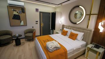 Ein Hotelzimmer mit einem Bett, zwei Sesseln, einem kleinen Tisch, einem Nachttisch mit Telefon und einem wandmontierten Spiegel.