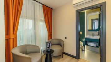 Habitación de hotel moderna con sofá, una mesita con una revista y vista al baño a través de una puerta de vidrio.