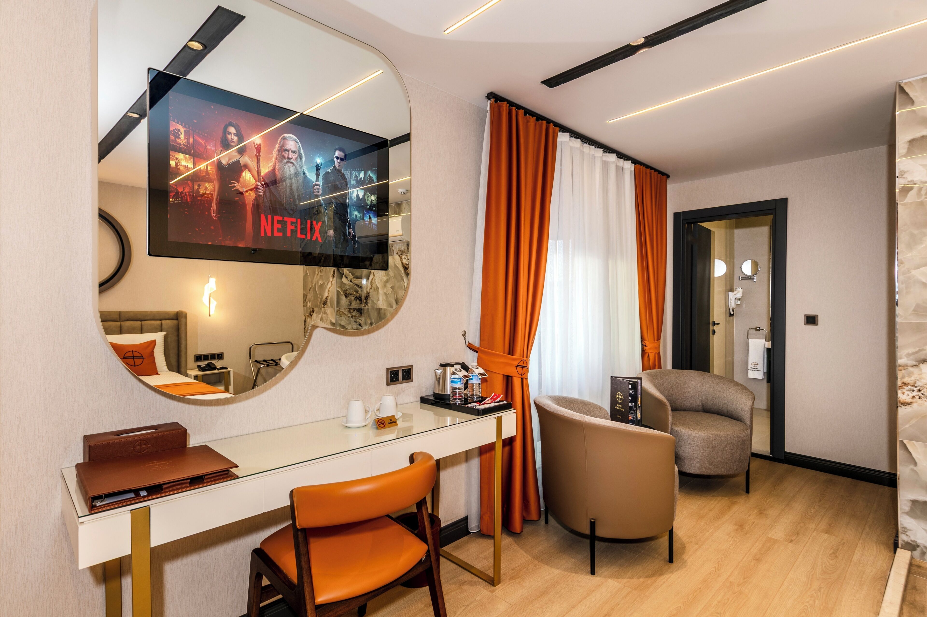 Habitació d'hotel amb un mirall gran, una taula de treball amb un ordinador portàtil, una cadira, un llit i un televisor que mostra una sèrie de Netflix.