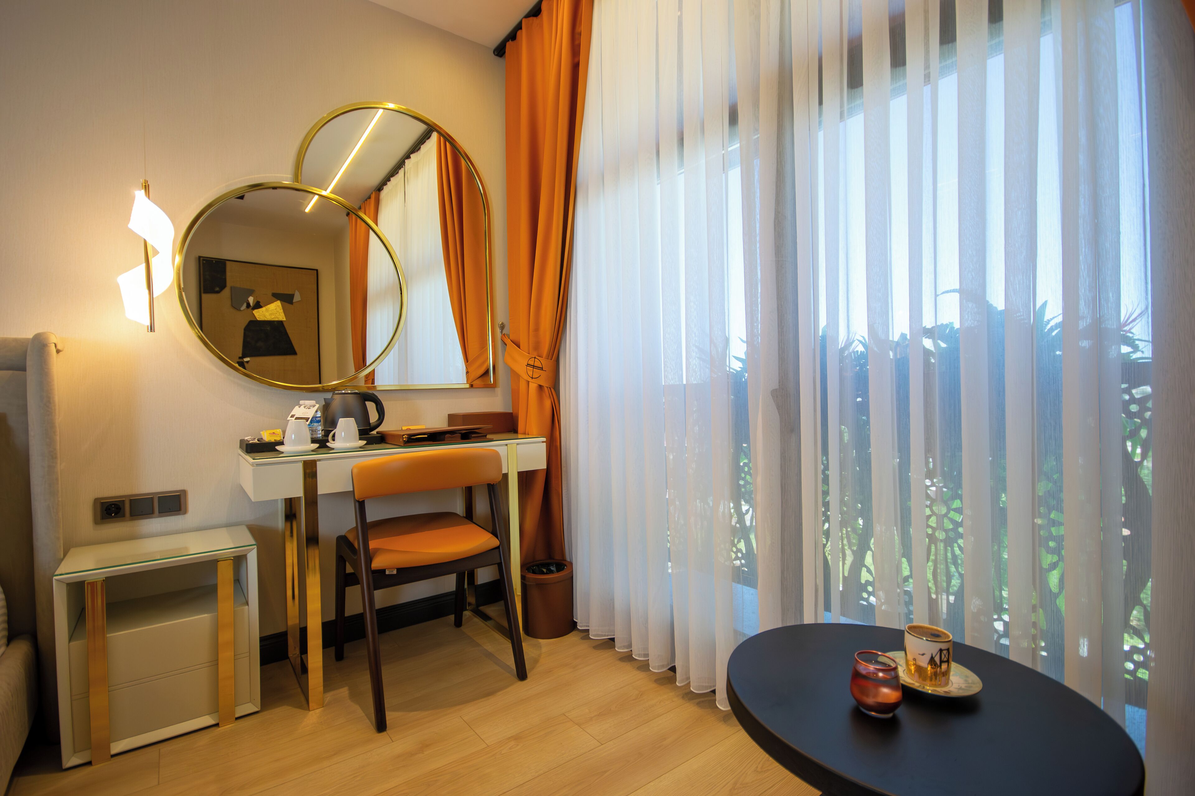 A hotel room with a desk, chair, and a round table with a cup and saucer.