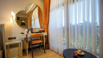 A hotel room with a desk, chair, and a round table with a cup and saucer.
